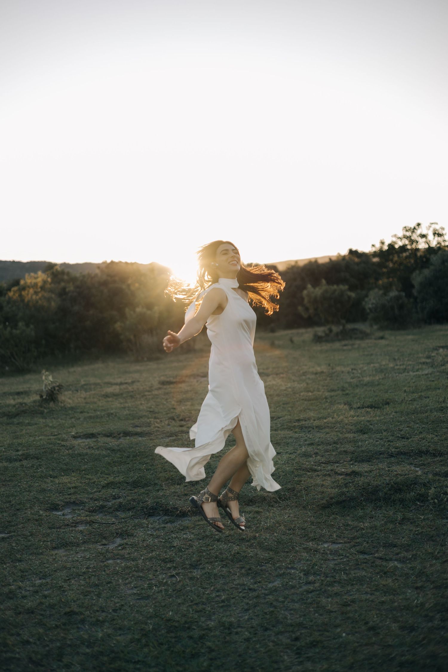 A person in a flowing white dress dances barefoot in a grassy field at sunset, their hair catching the golden light.