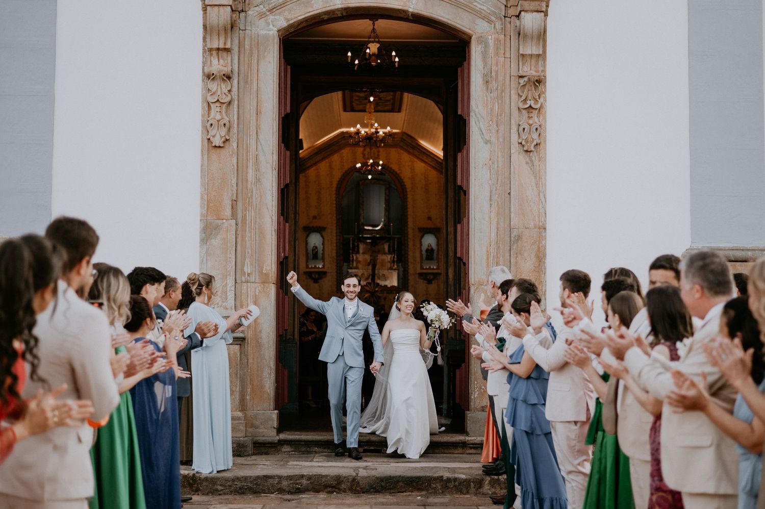 Wedding guests line the church entrance throwing petals as newlyweds exit the ceremony.