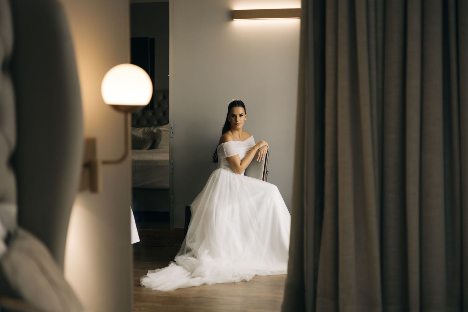 A wedding dress captured in a moody hotel room setting with dramatic lighting.