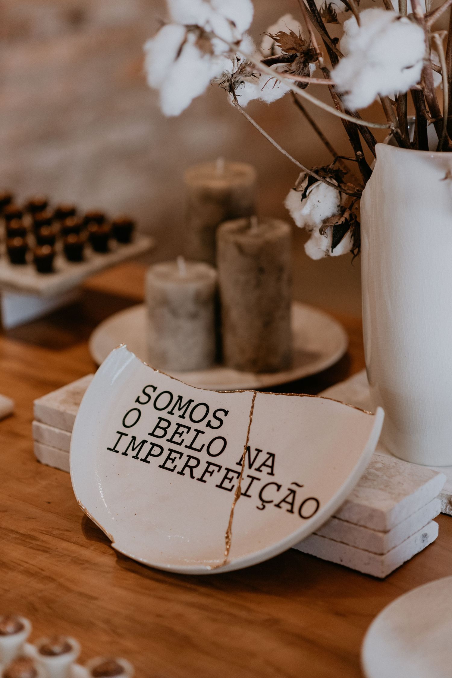 Portuguese quote on ceramic plate with cotton stems and candles in warm tones.