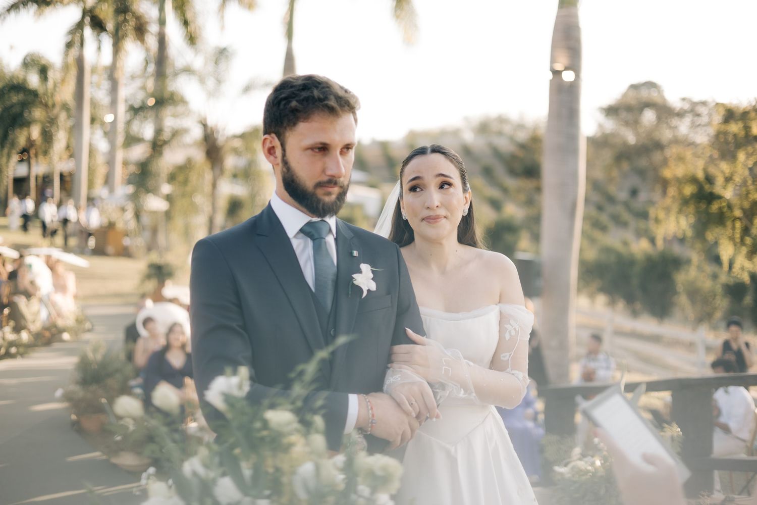 Romantic outdoor wedding couple embracing in a tropical garden setting with palm trees at sunset.