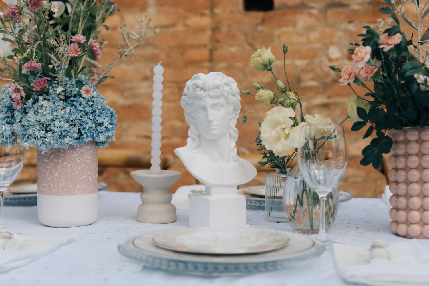 Classic white bust statue centerpiece with delicate floral arrangements and candles on elegant table setting.