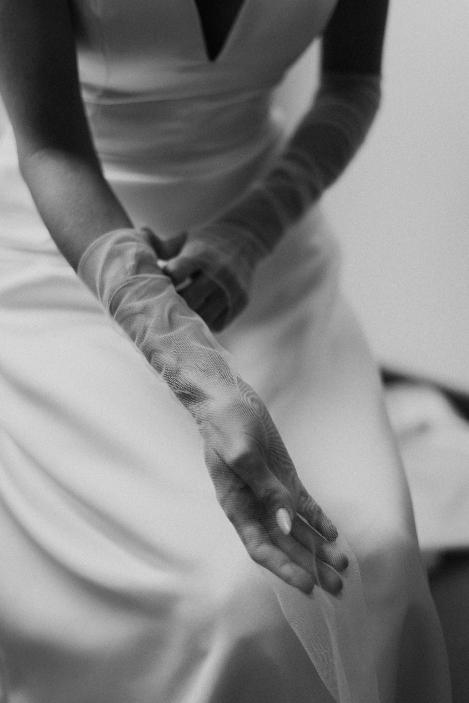 Close-up view of delicate white lace gloves on a bride's hands against a white wedding dress background.