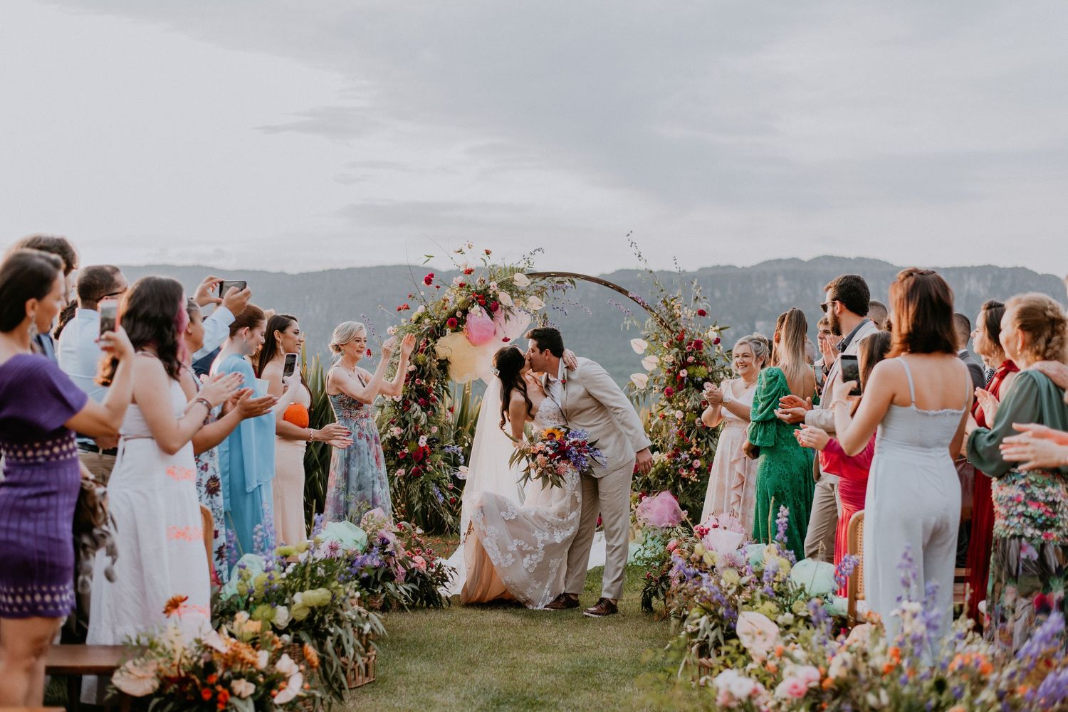 Wedding ceremony under floral arch overlooking mountain vista with guests in attendance.