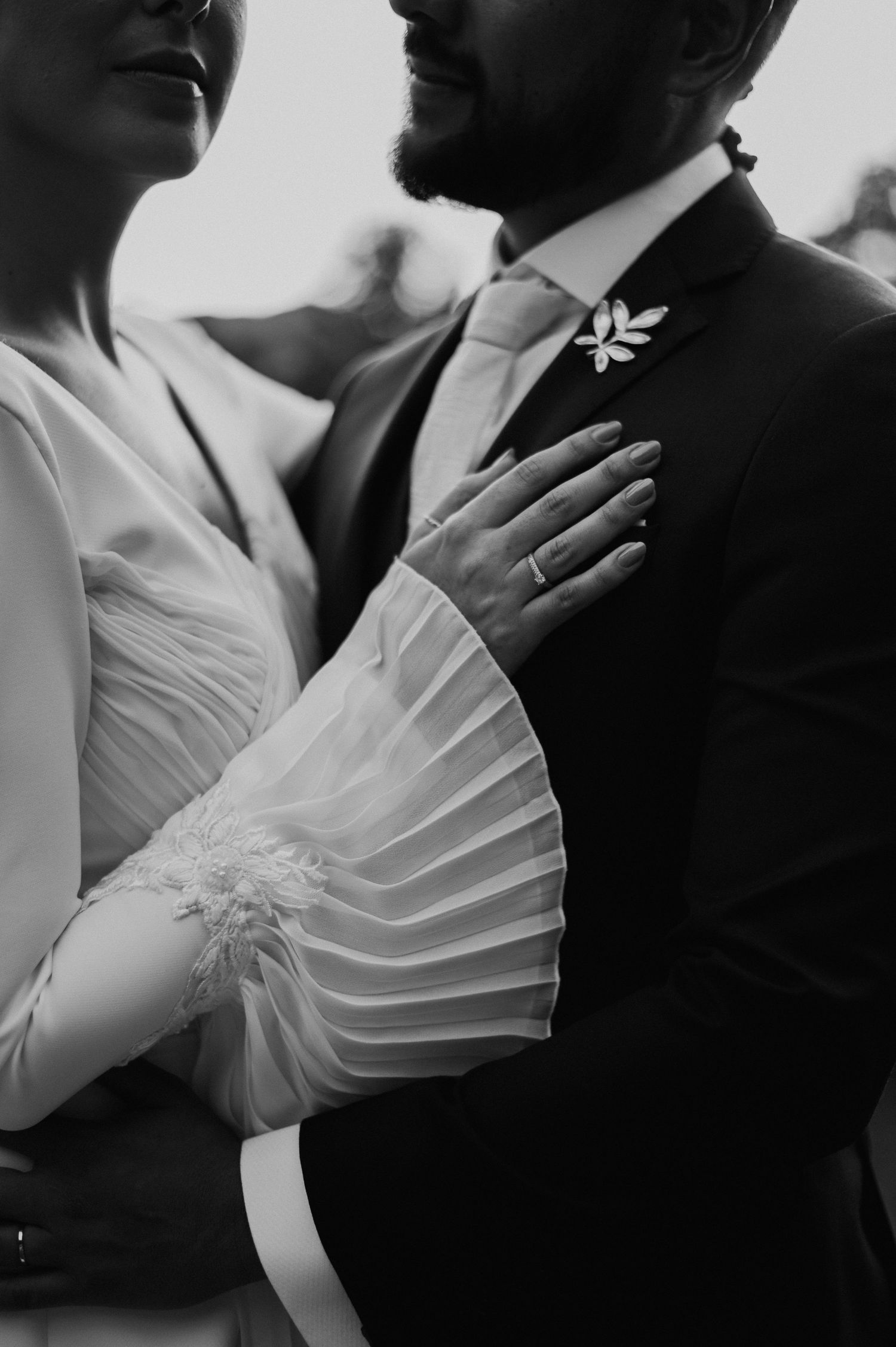 Intimate black and white portrait showing bride's pleated sleeve detail and groom's boutonniere.