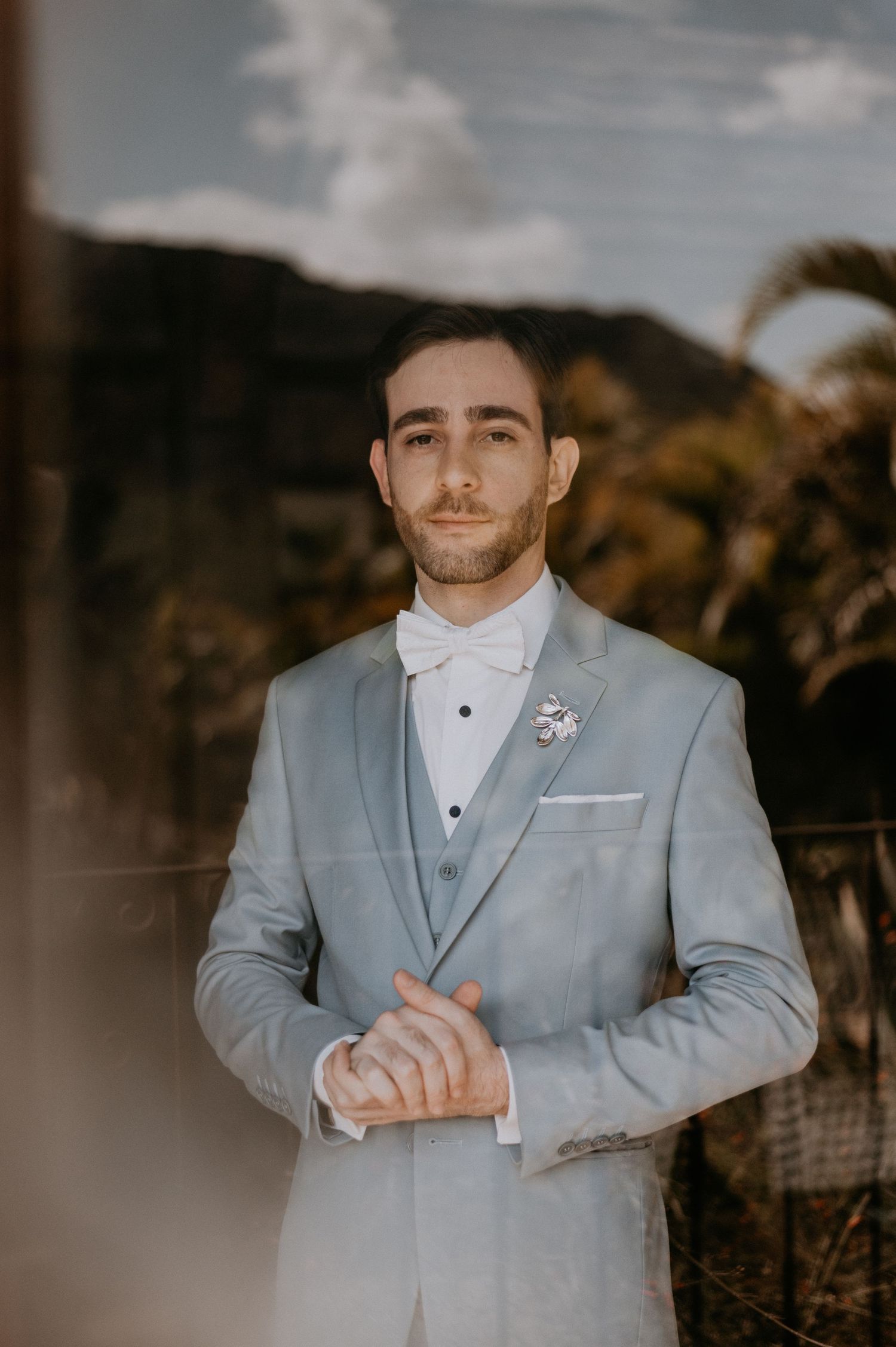 Formal portrait of groom in light grey three-piece suit with mountain landscape backdrop.
