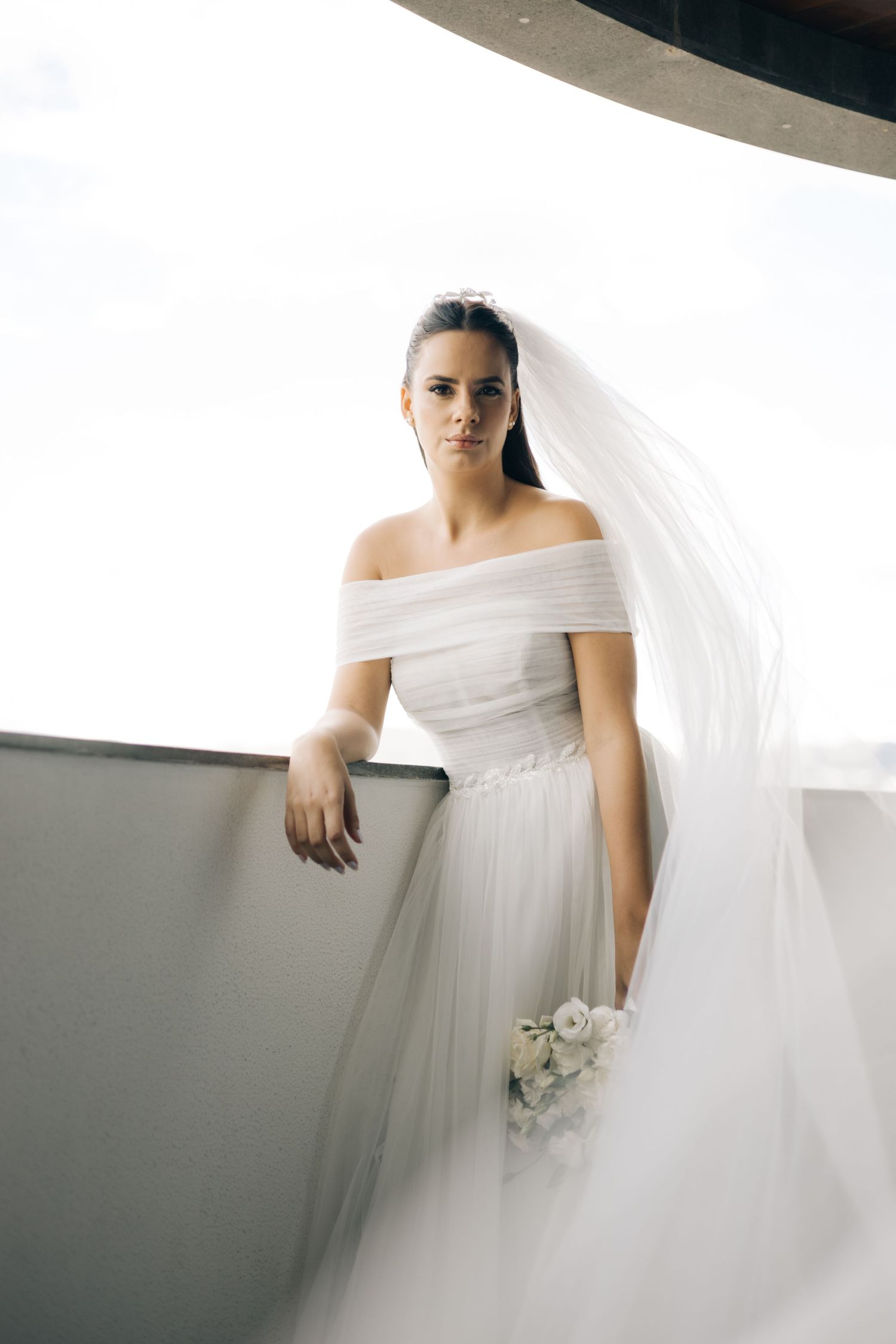 Full-length bridal portrait on a balcony with flowing veil and white bouquet.