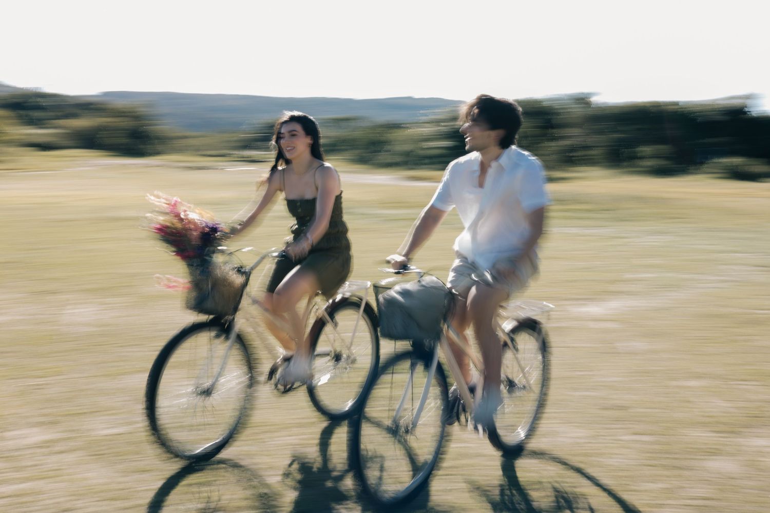 Cyclists ride together on bikes through sunny countryside with motion blur effects in background.