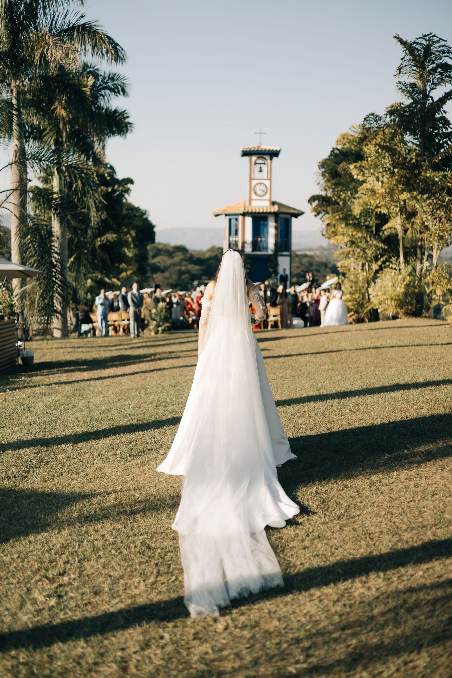 A flowing white wedding veil trails on the ground with a clock tower and palm trees in the background.