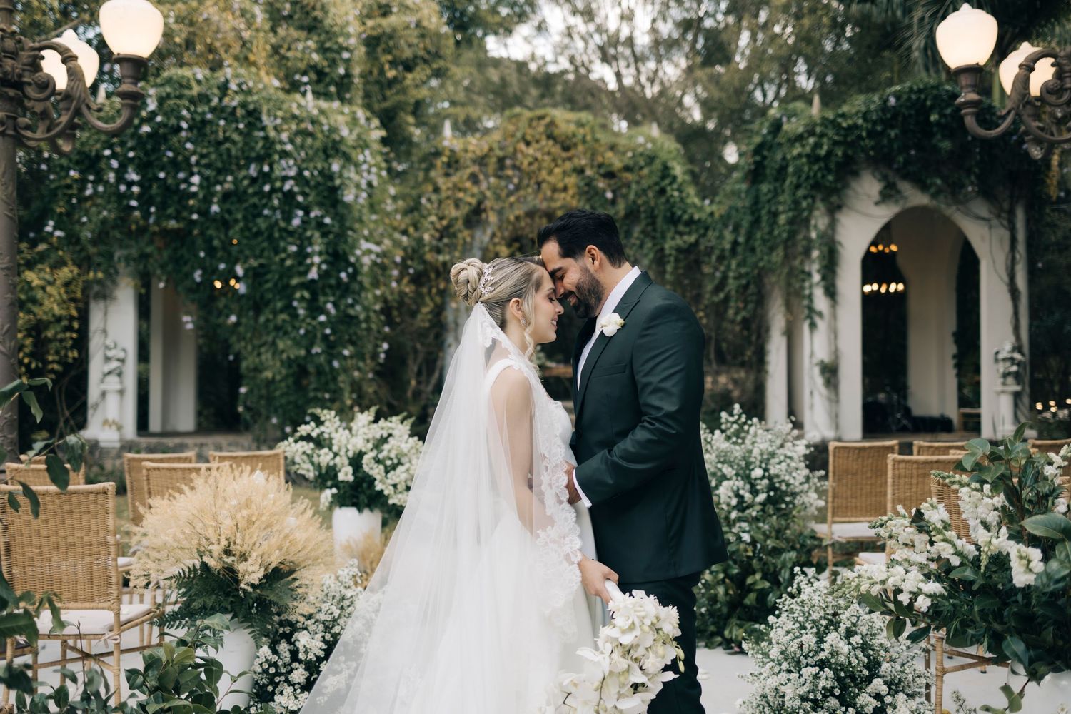 Elegant garden wedding setting with floral arch, vintage lamps and romantic landscaping creating an intimate atmosphere.