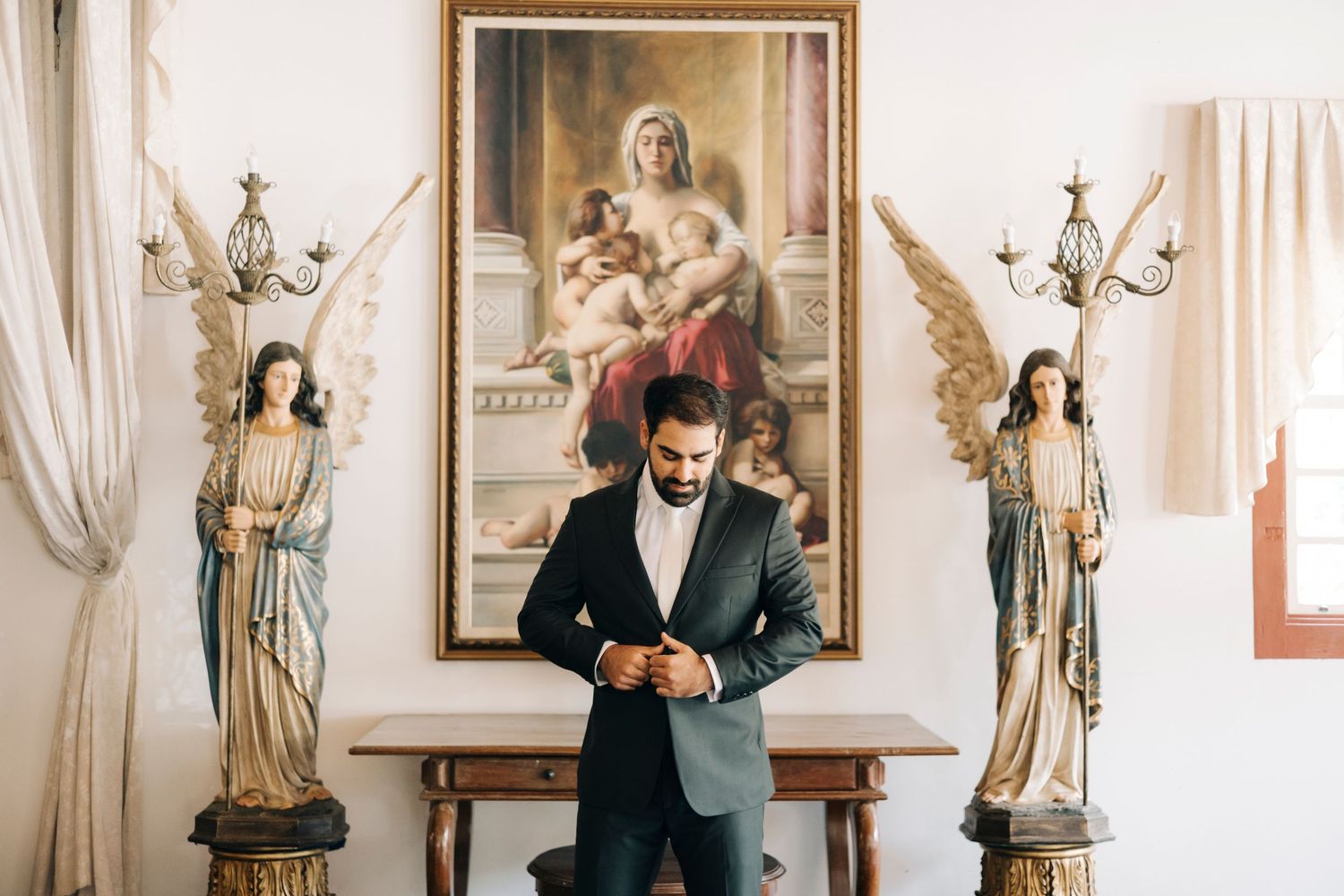 Person in formal attire checking phone while standing against wall with ornate decor and artwork.