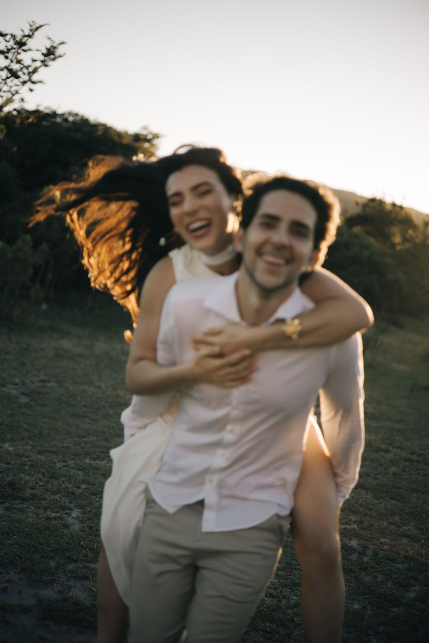 A couple shares a joyful moment outdoors during sunset with warm backlighting creating a romantic atmosphere.