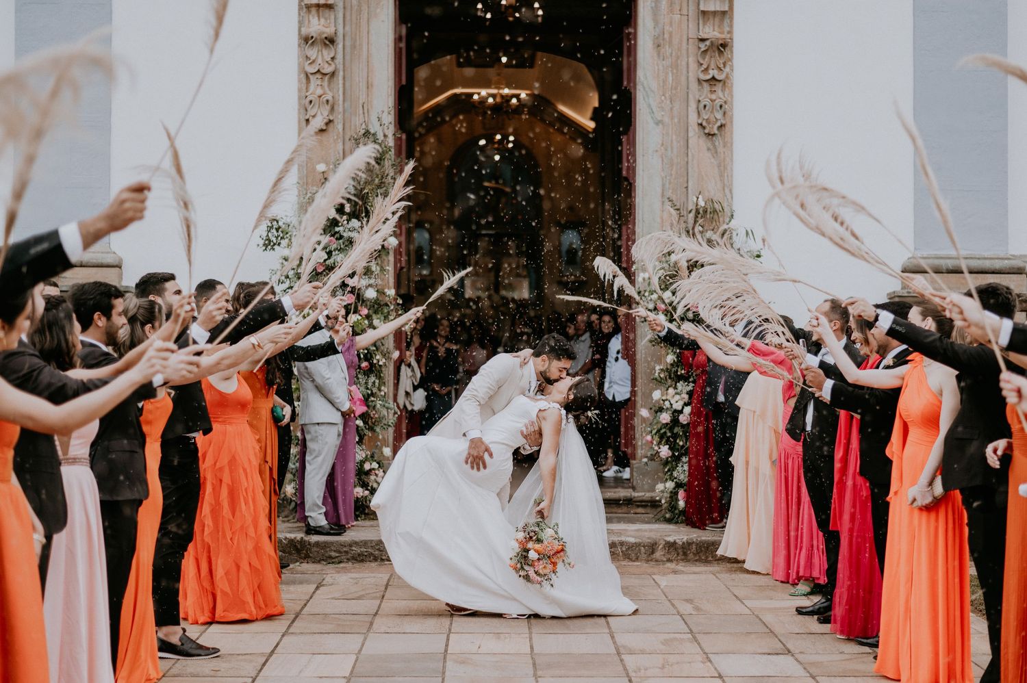 Wedding exit with guests in colorful dresses throwing petals outside church entrance.