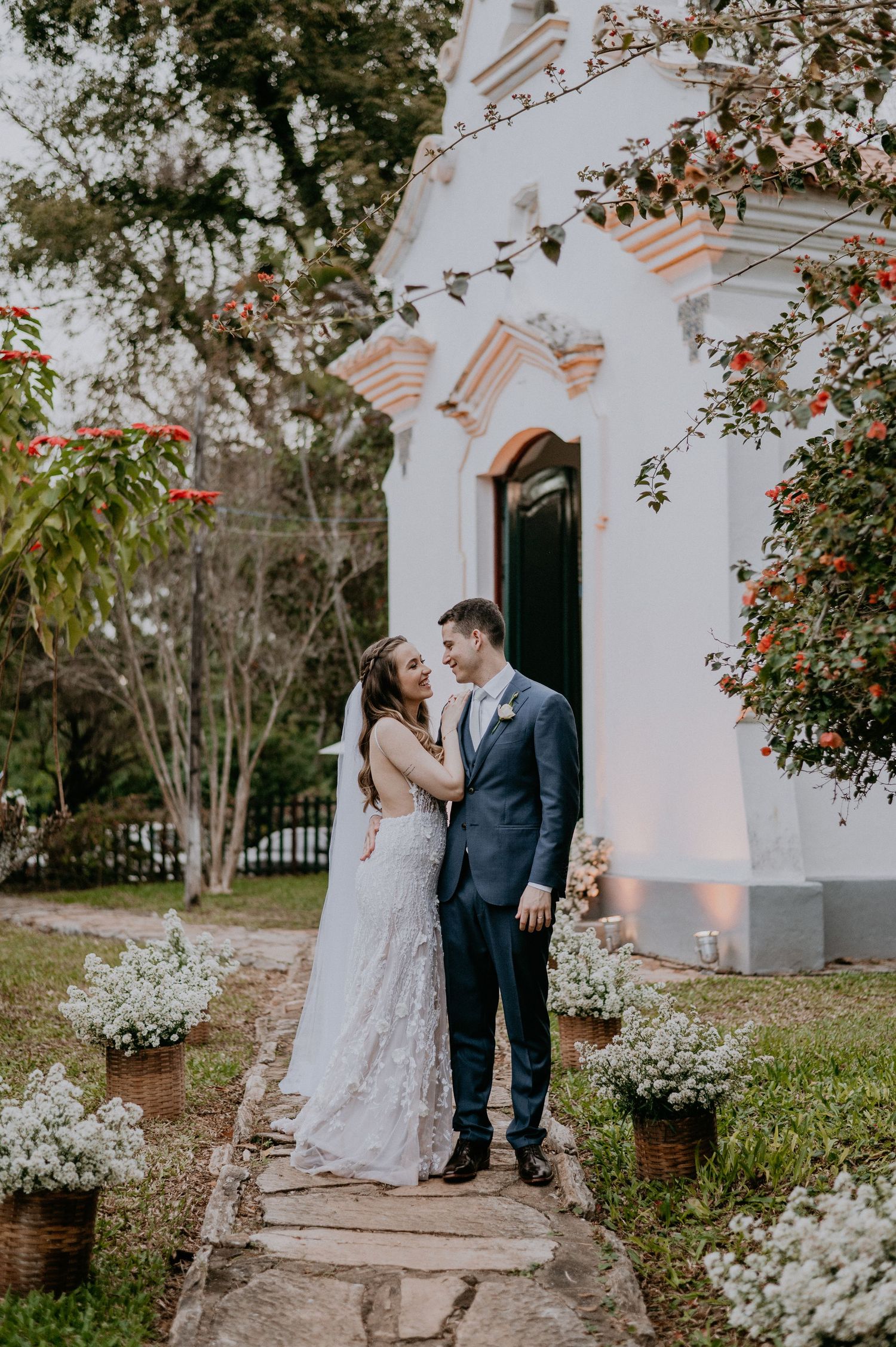 Romantic wedding couple posing outside white chapel with floral decorations.