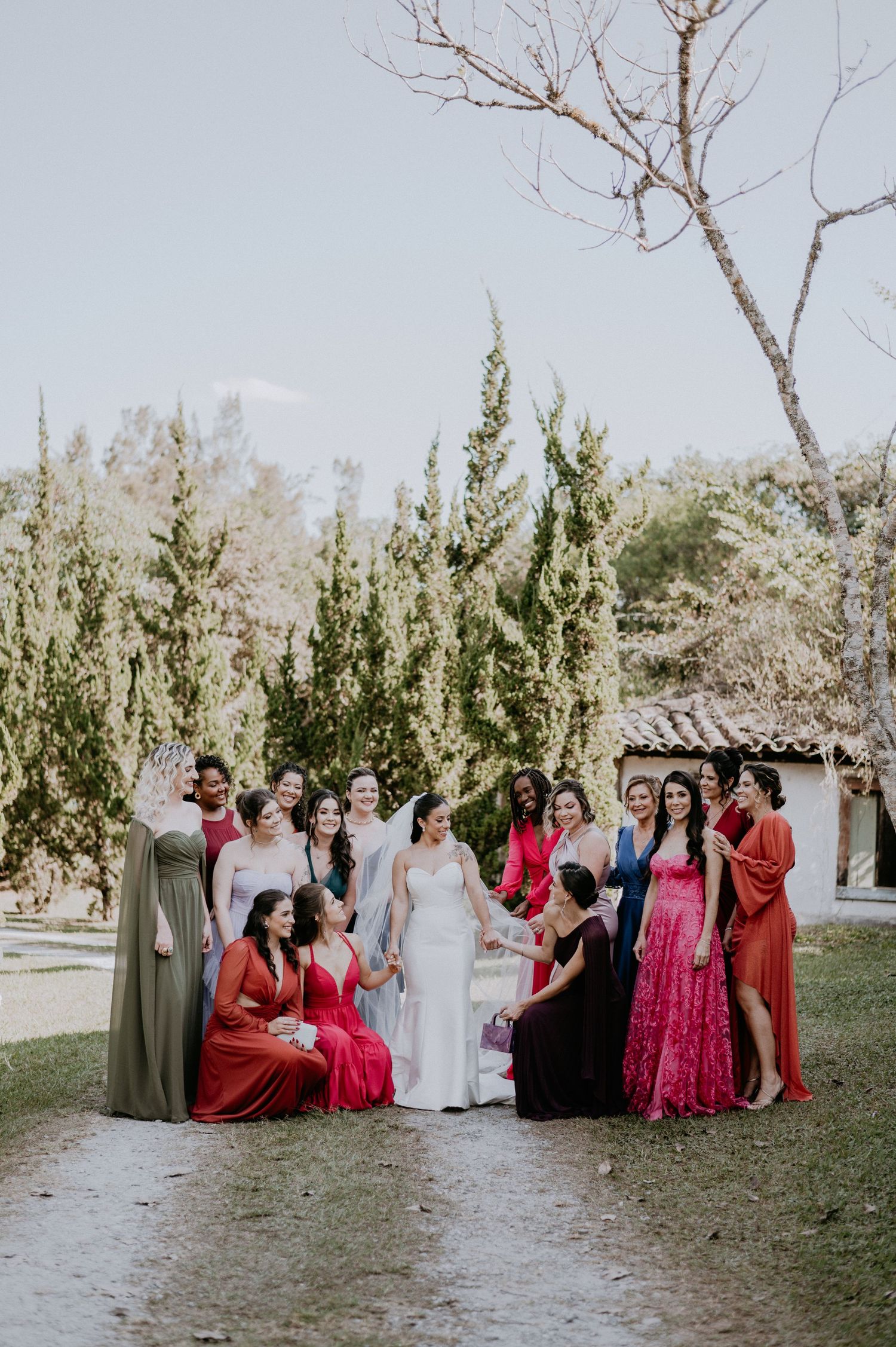 Wedding party gathered on garden path wearing colorful formal dresses.