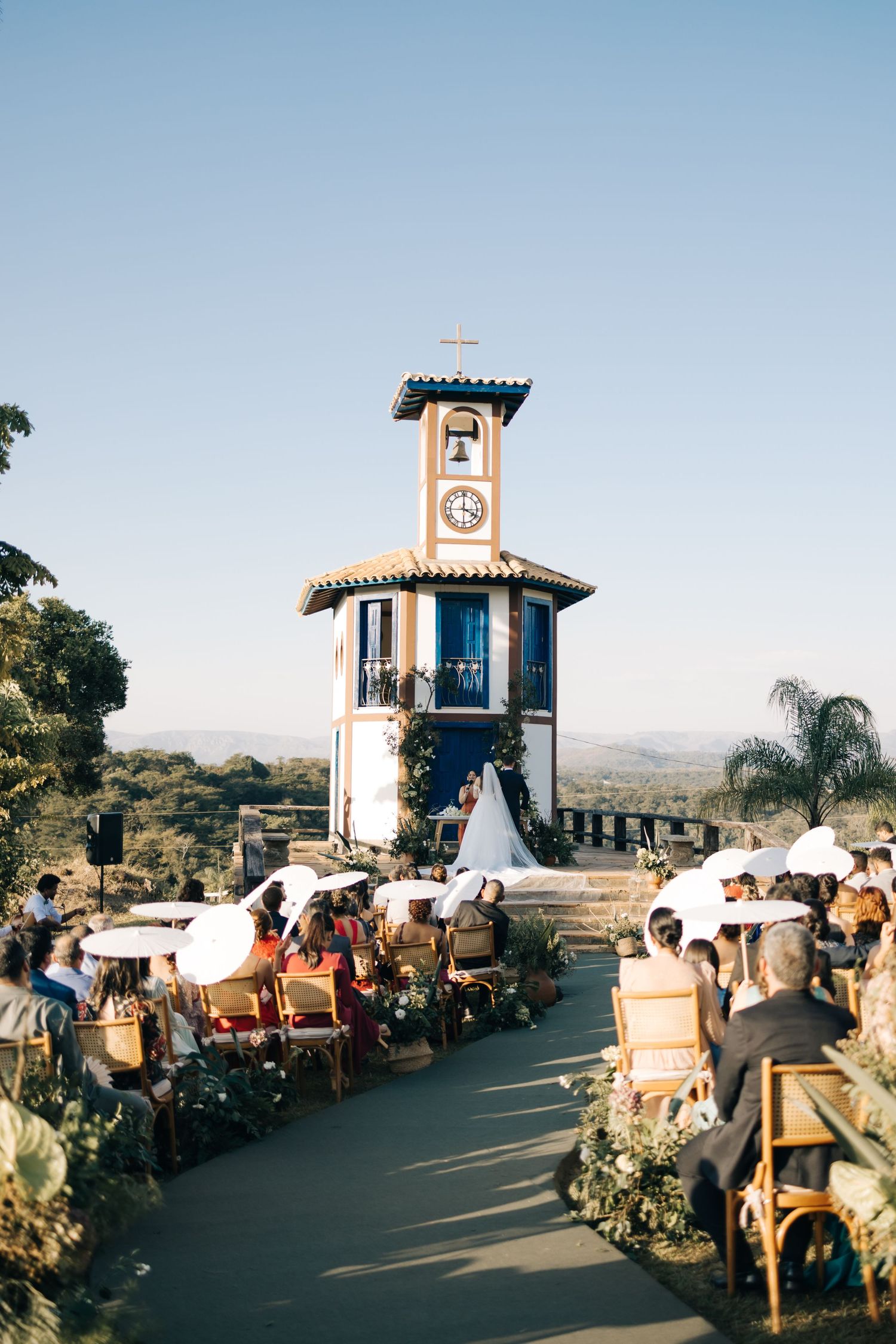 An outdoor wedding ceremony setup with rows of chairs facing a charming white clock tower under a clear blue sky.