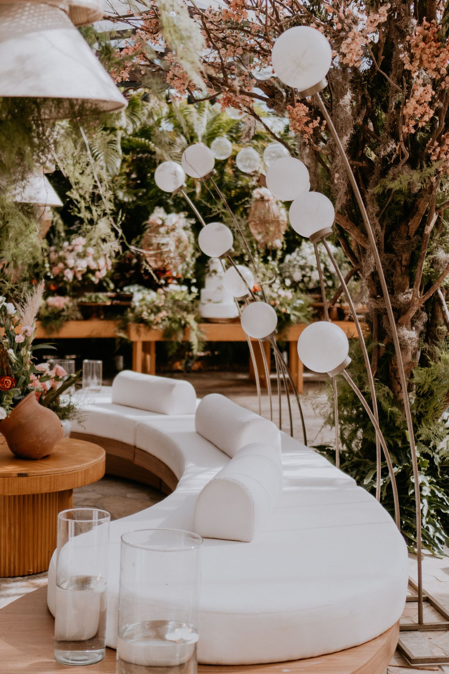 Modern outdoor lounge setup with white curved seating and hanging paper lanterns.