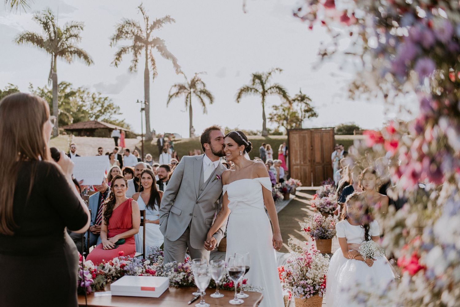 Outdoor wedding reception with palm trees and pink floral decorations.