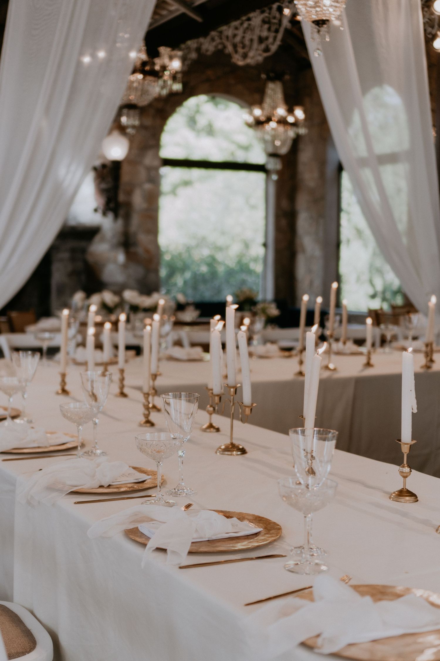 Elegant table setting with white linens, gold chargers, and tall white tapered candles.