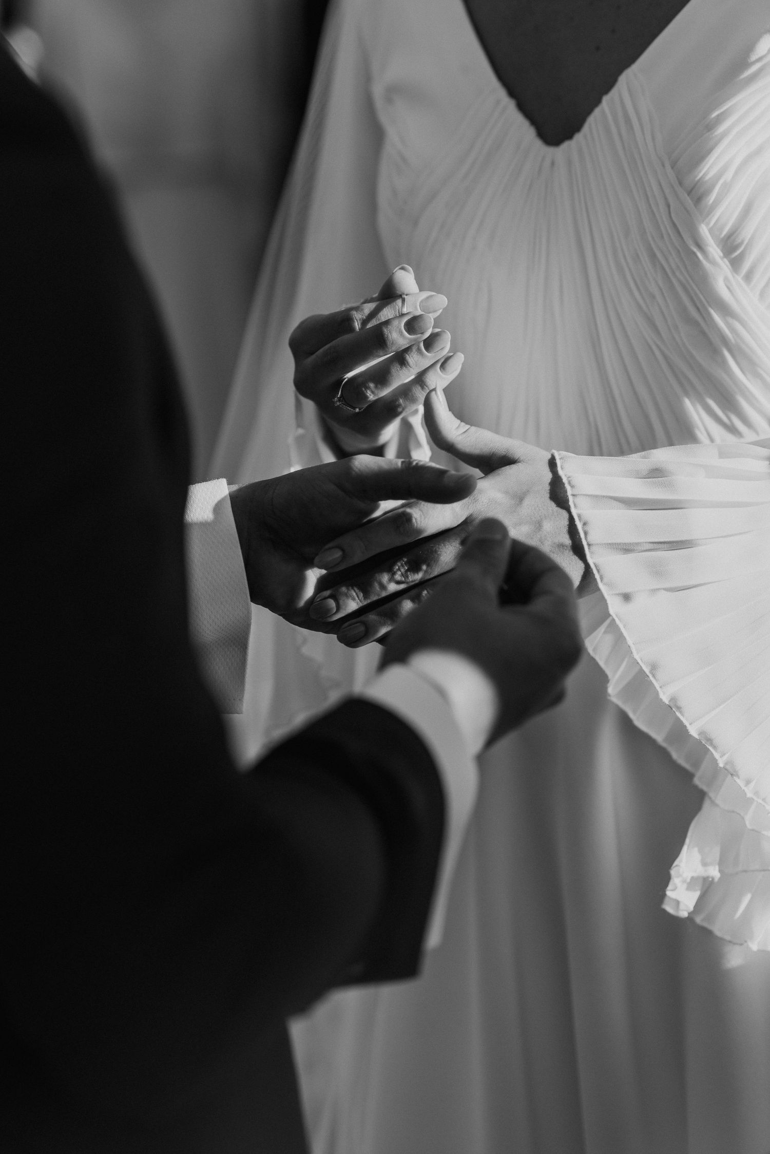 Black and white close-up of couple exchanging rings during wedding ceremony.