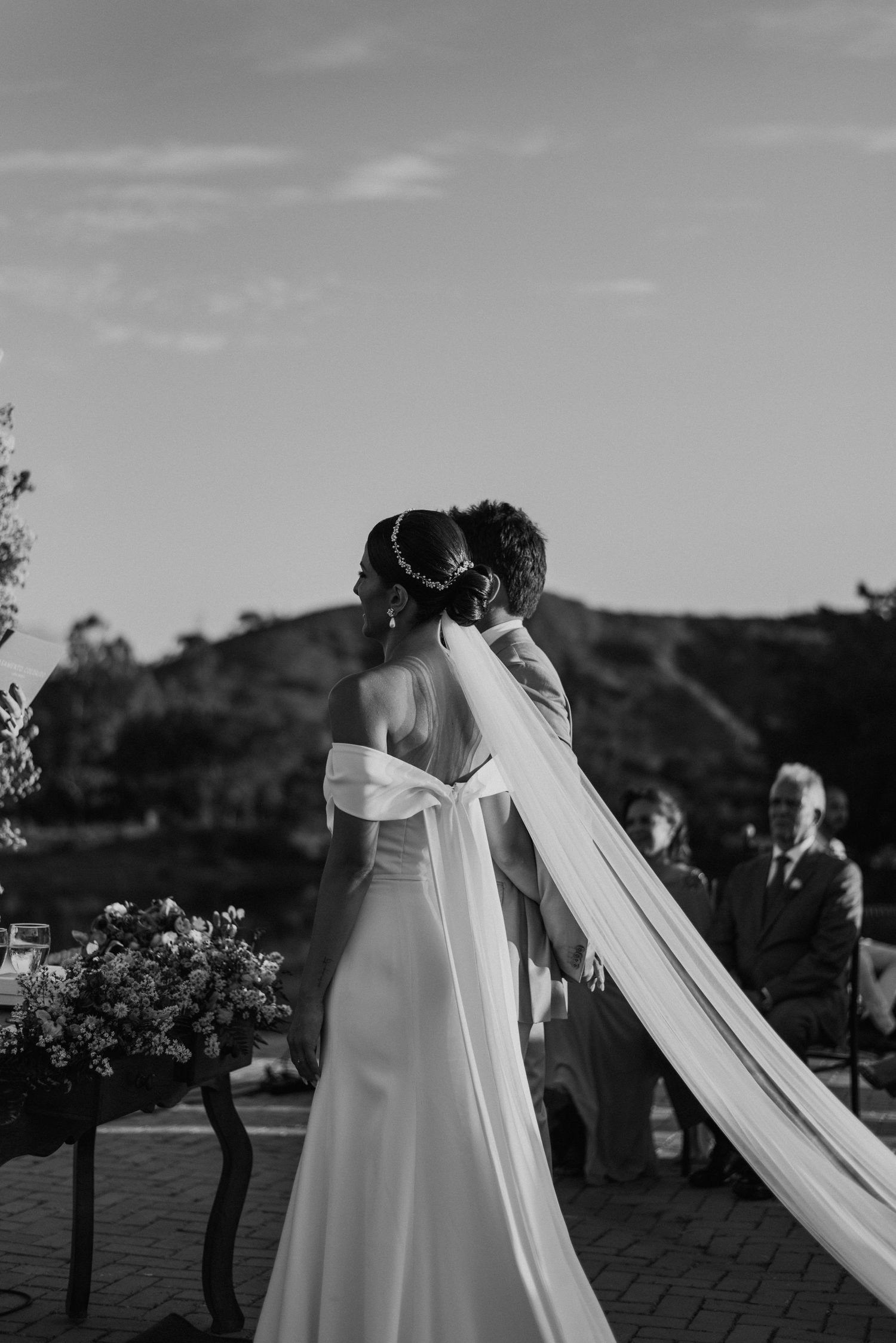 Black and white portrait of bride in flowing veil during outdoor ceremony.