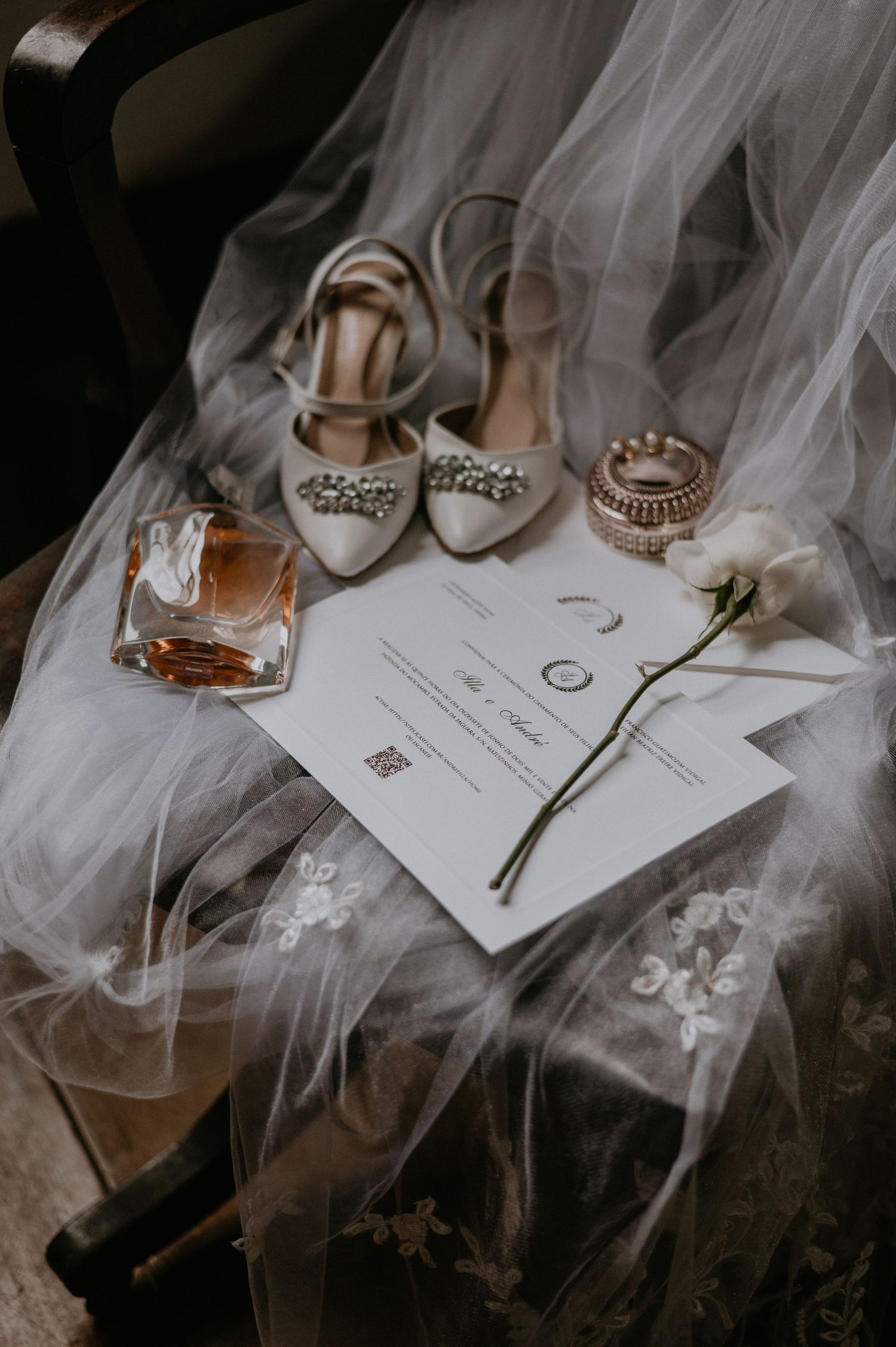 Wedding details flatlay with bridal shoes, perfume, invitation and veil on dark background.