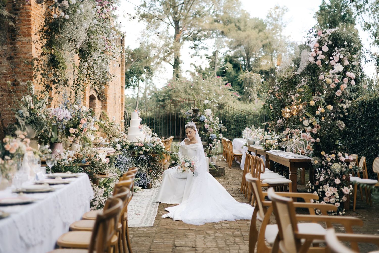 An elegant outdoor wedding reception setup with floral decorations and wooden chairs in a garden setting.