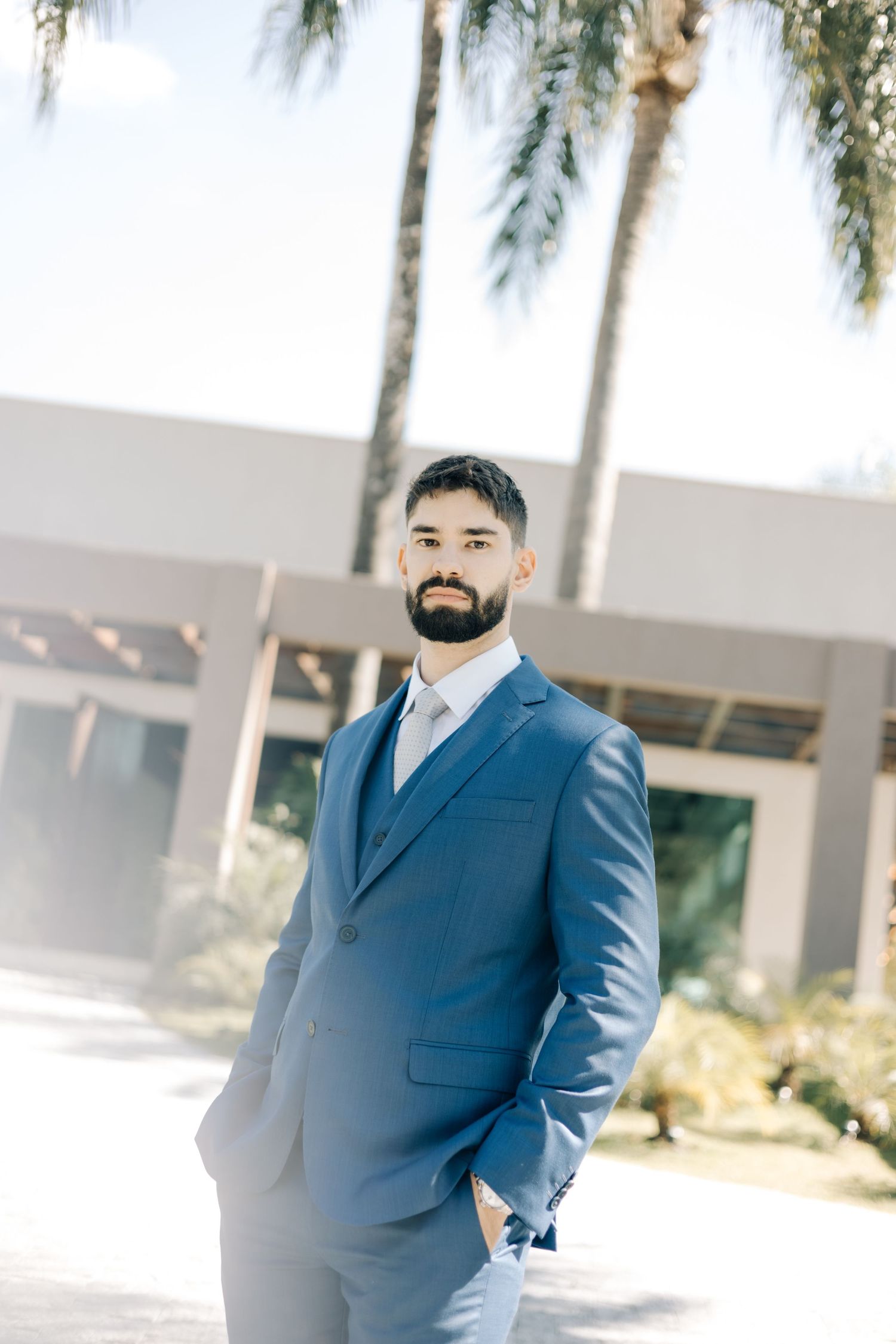 Portrait of a groom in a stylish blue suit standing outdoors with palm trees in the background.