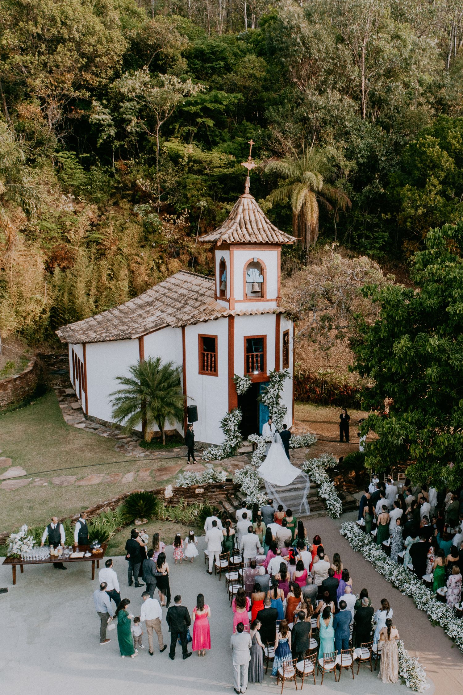 Aerial view of white chapel wedding ceremony surrounded by lush tropical gardens.