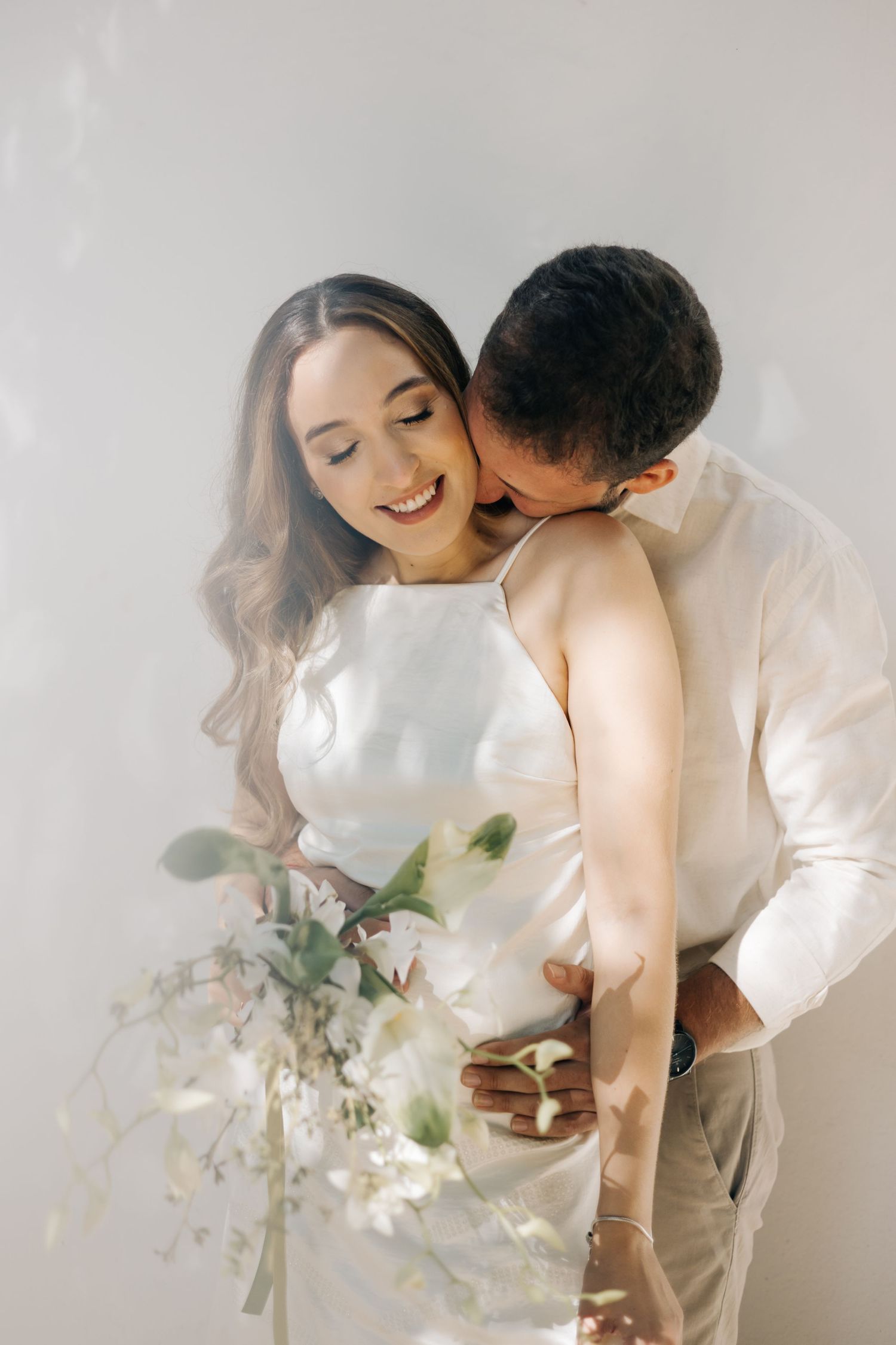 Romantic bridal portrait against white background with delicate white floral bouquet and intimate embrace.