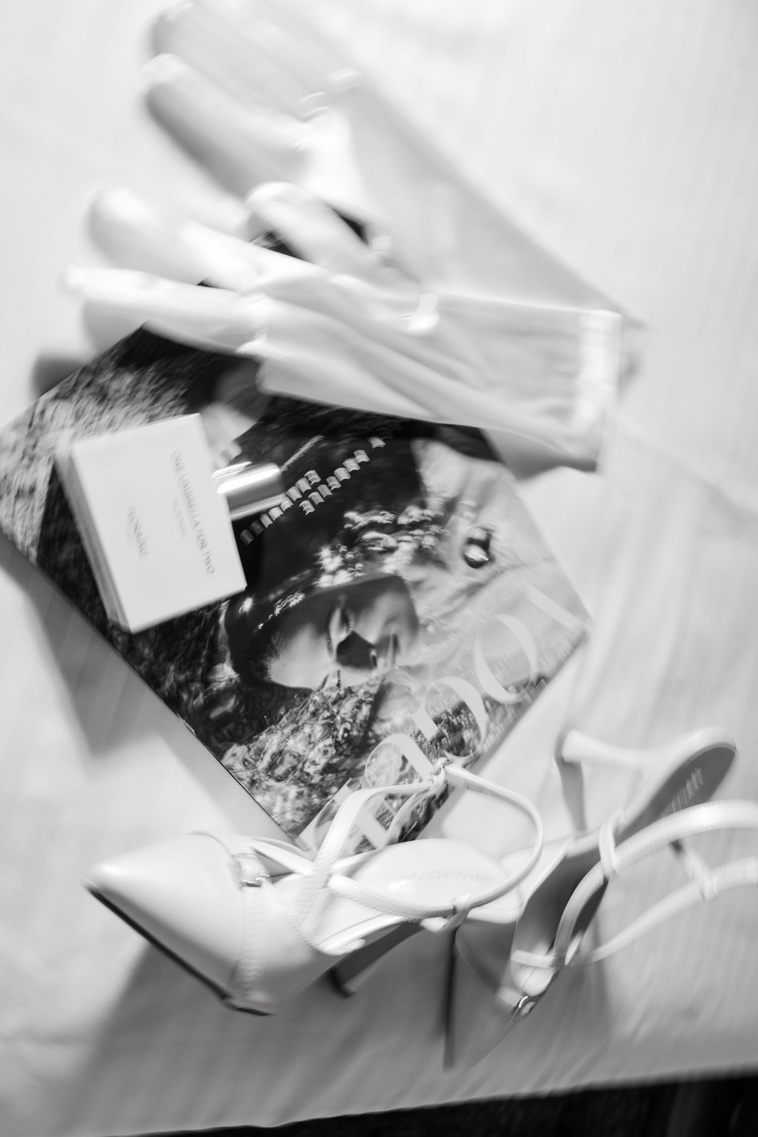 Black and white flat lay of bridal accessories including white heels and magazine.