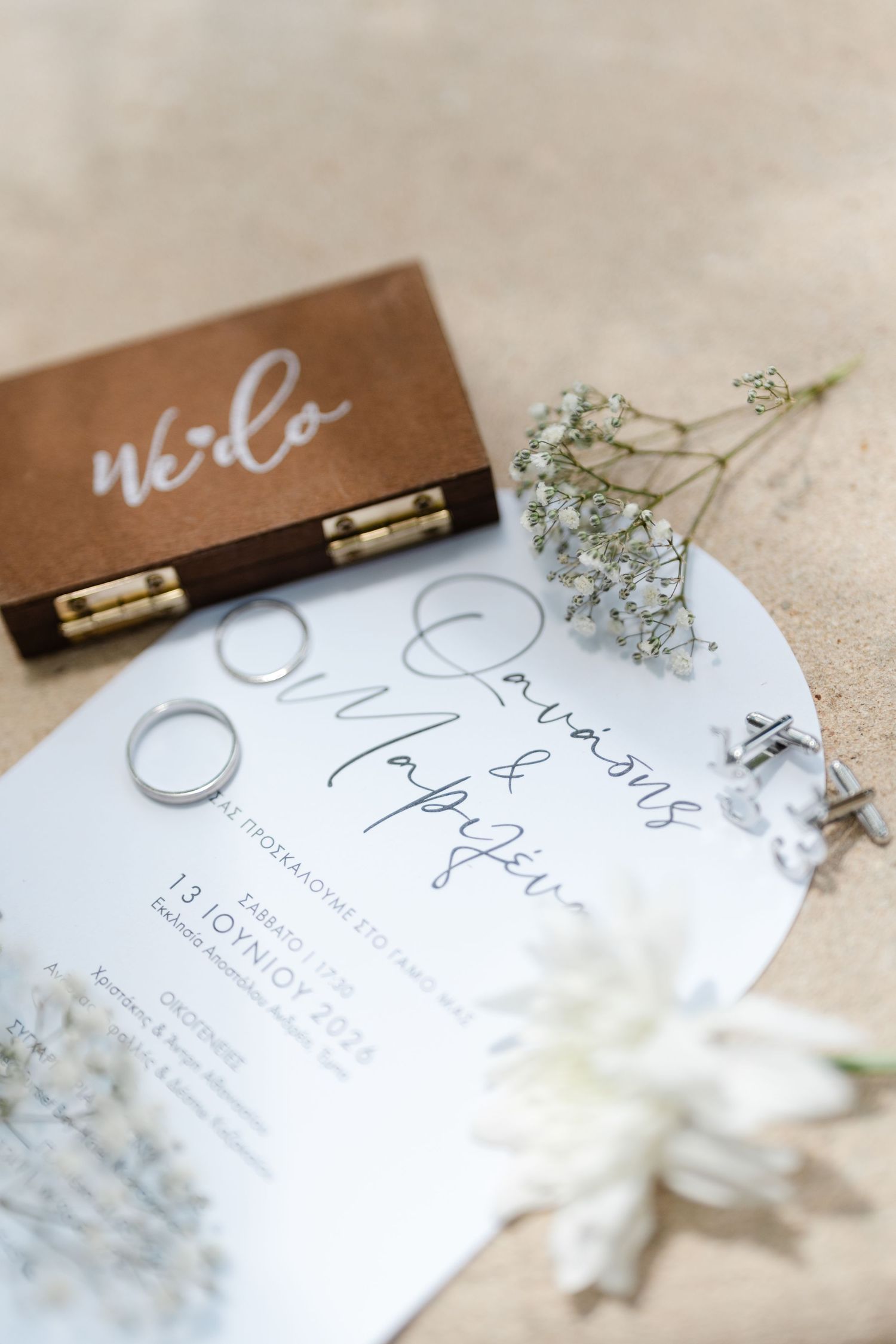 Wedding stationery flat lay with ring box, silver bands, white flowers, and elegant invitation card.