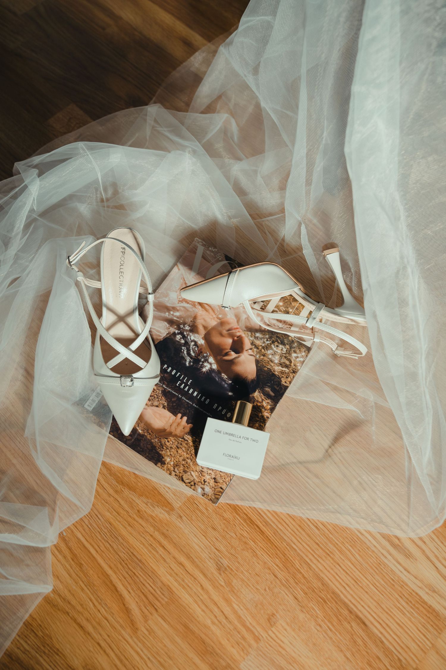 White bridal heels and wedding veil arranged with magazine on wooden floor.
