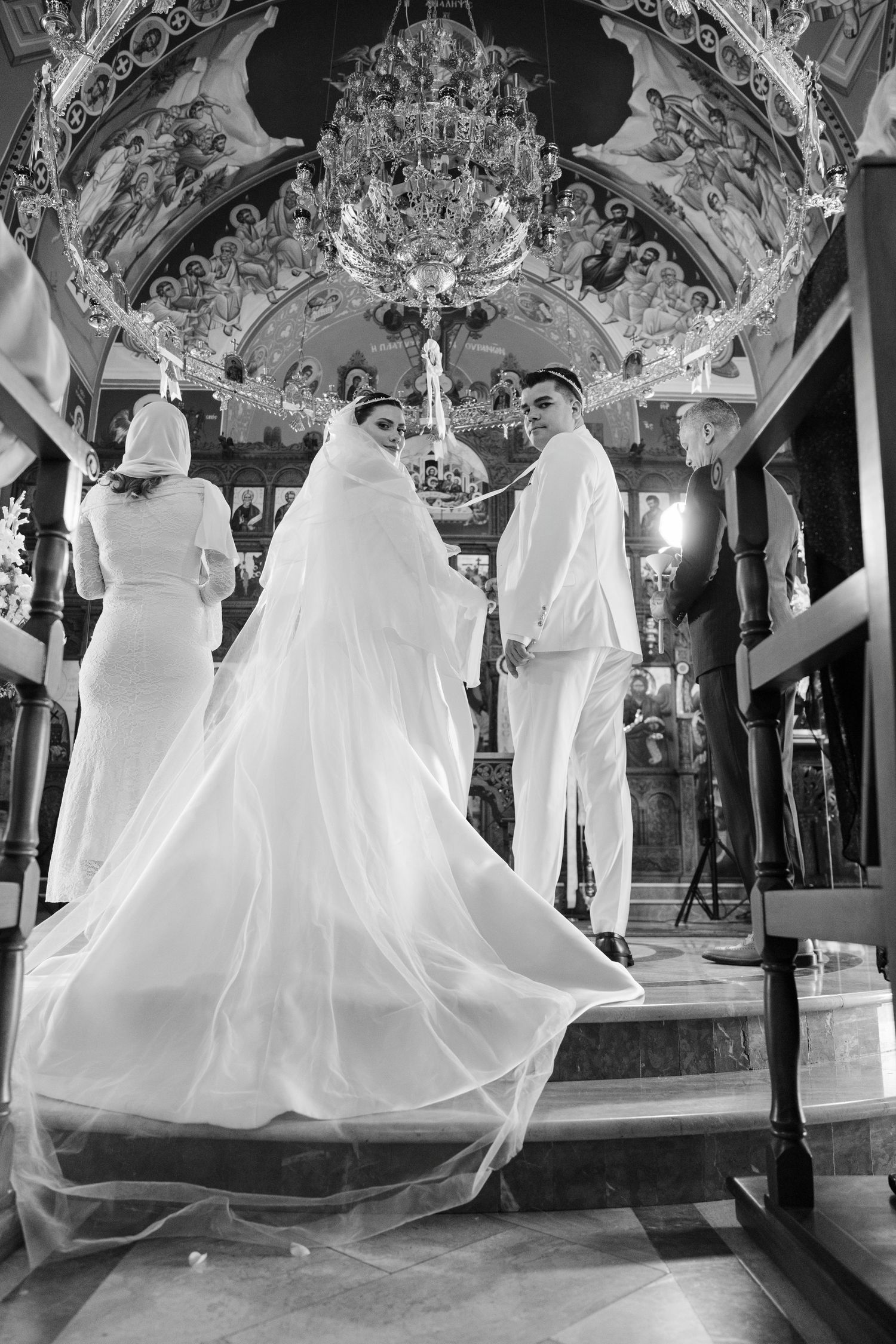 Bride and groom at ornate church altar with stunning chandelier and frescoes above.