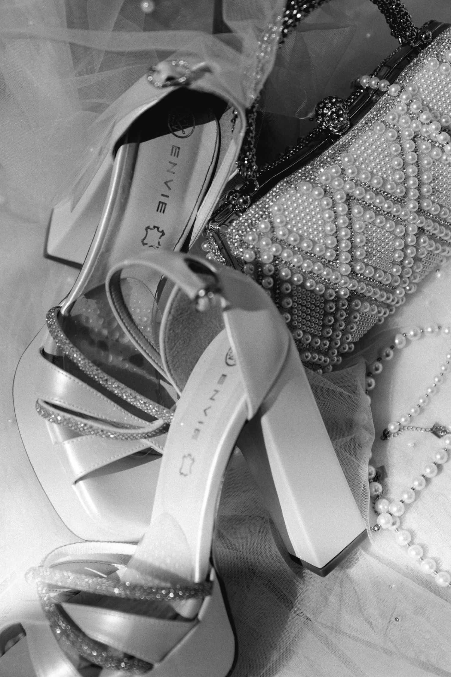 Bridal accessories flat lay featuring white heeled sandals, pearl necklace, and beaded clutch bag.