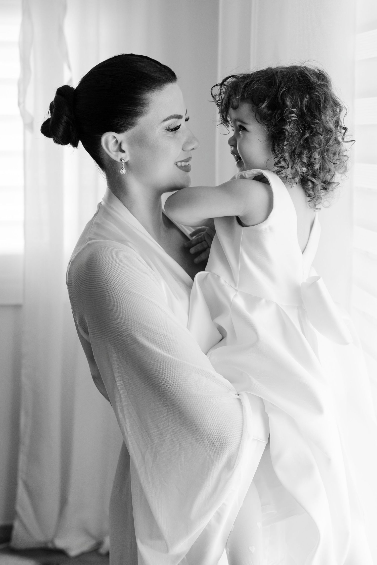 Black and white photo of a bride in white robe tenderly holding a curly-haired child.