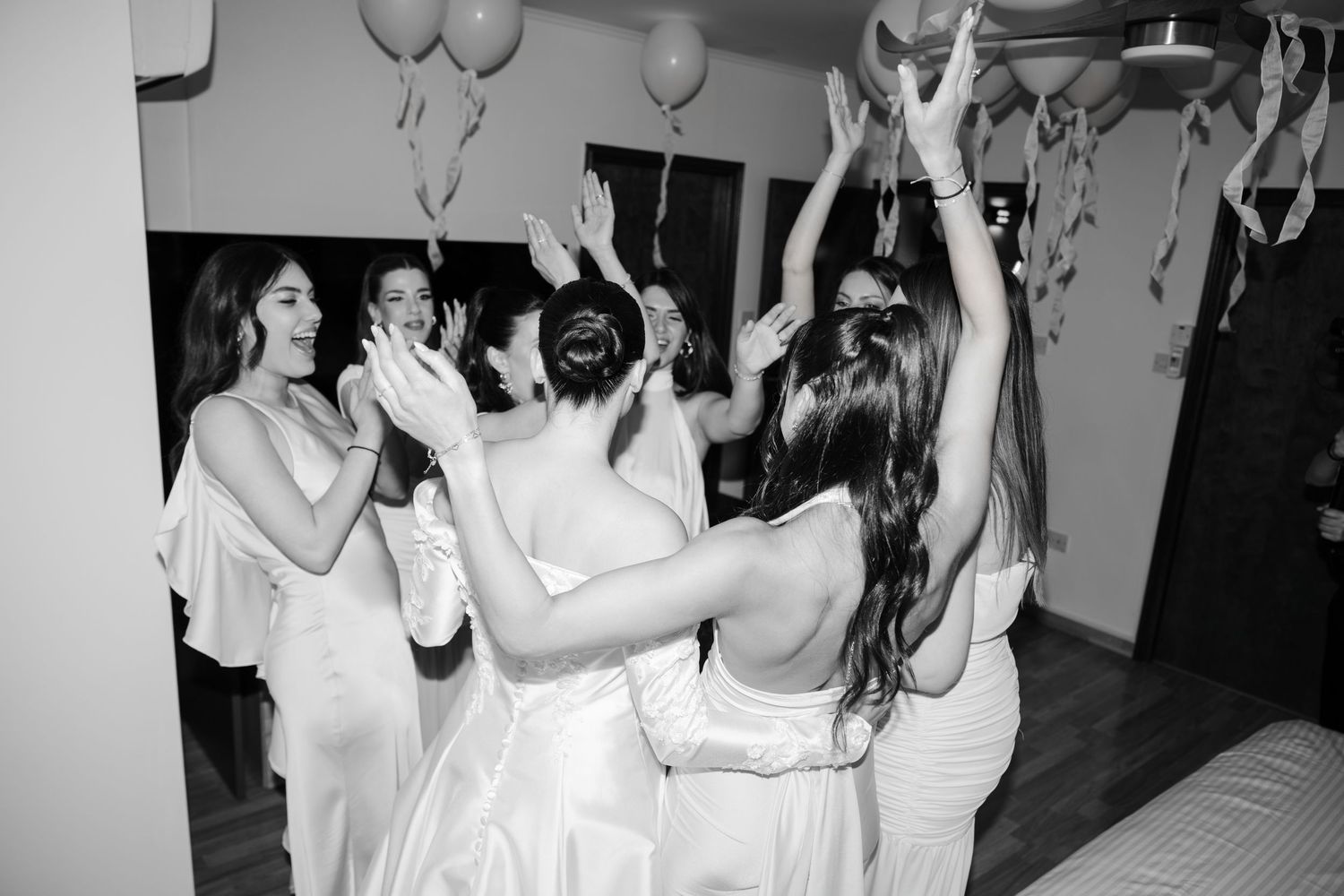 Black and white photo of bride and bridesmaids dancing joyfully during wedding preparations.