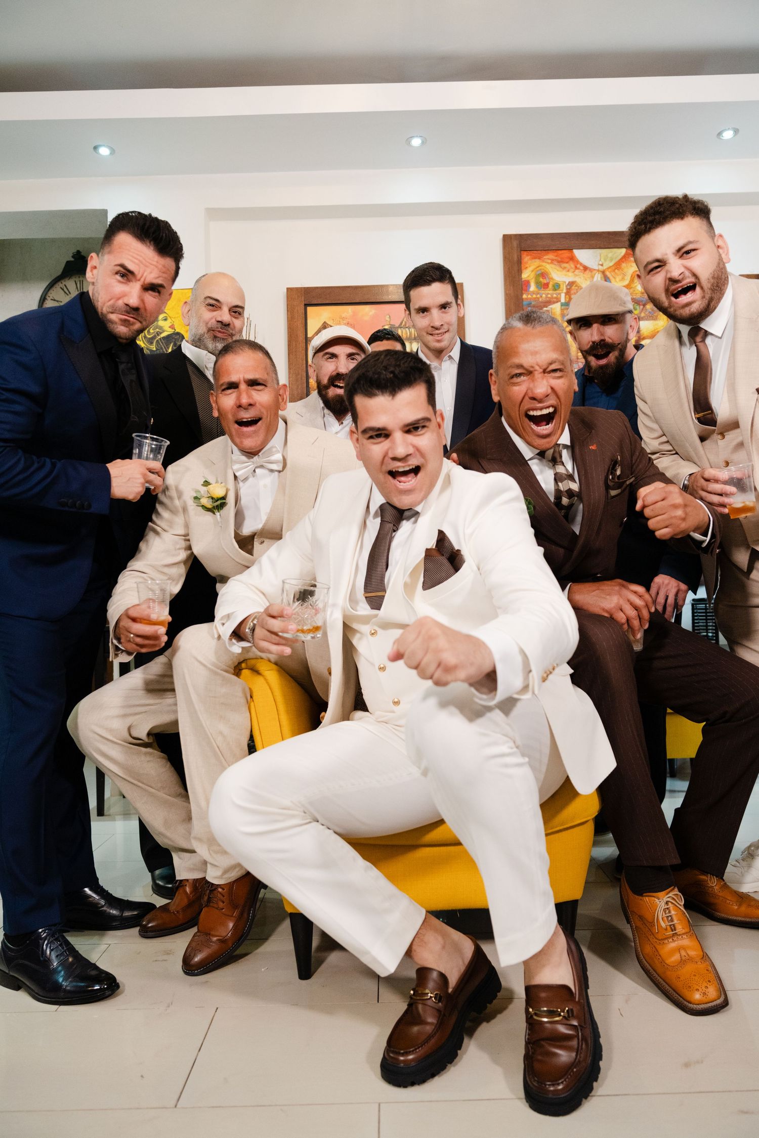 Excited groom celebrates with groomsmen in stylish suits at pre-wedding gathering indoors.