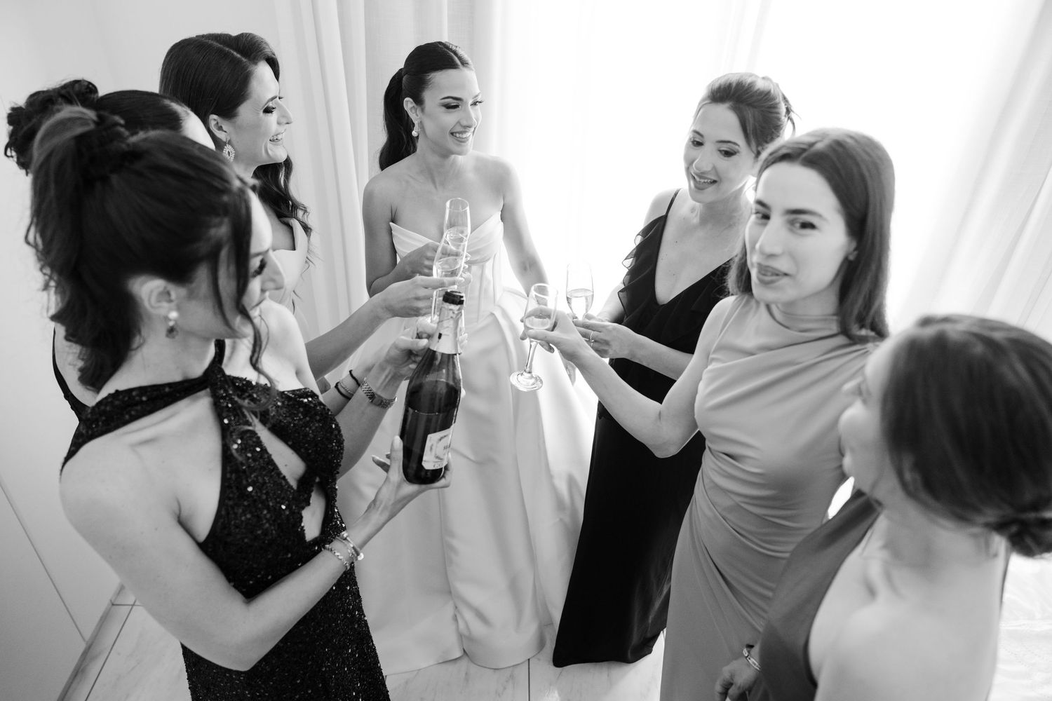 Black and white photo of bride and bridesmaids toasting with champagne glasses.