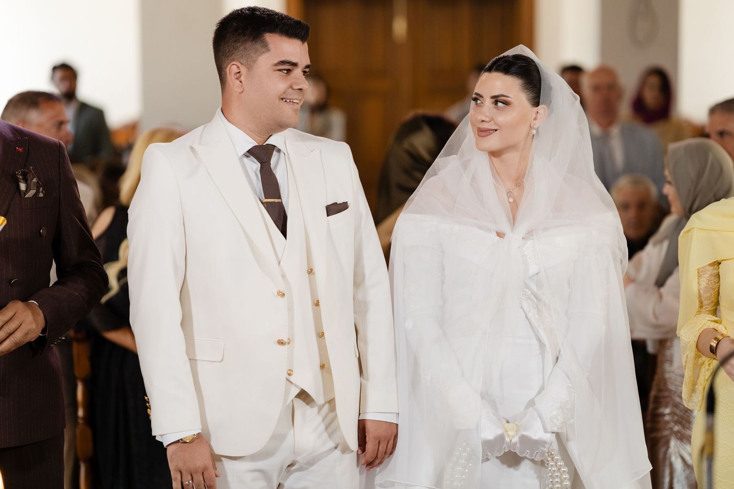 Bride and groom in white attire walking down church aisle during wedding ceremony.
