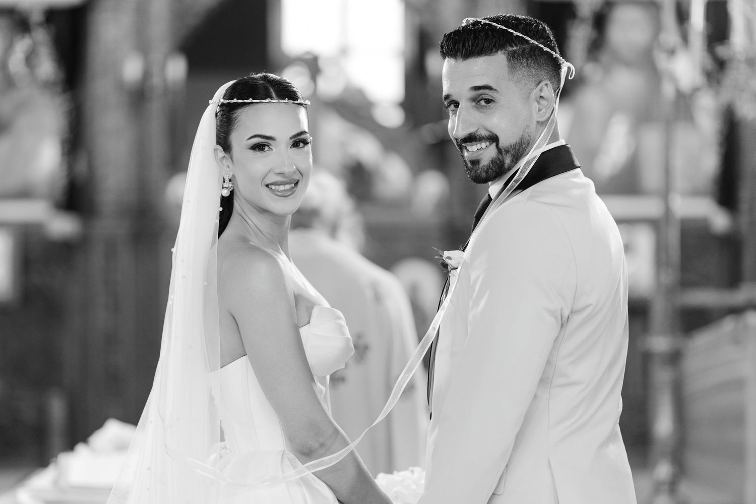Smiling bride and groom hold hands during wedding ceremony in black and white photo.