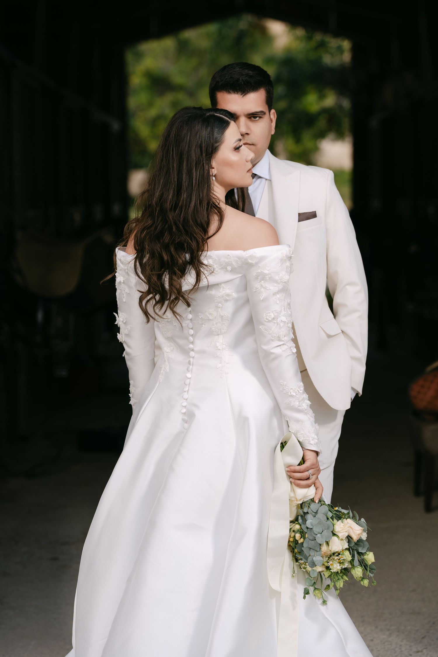 Bride and groom sharing a kiss while she holds a white bouquet in a romantic archway.