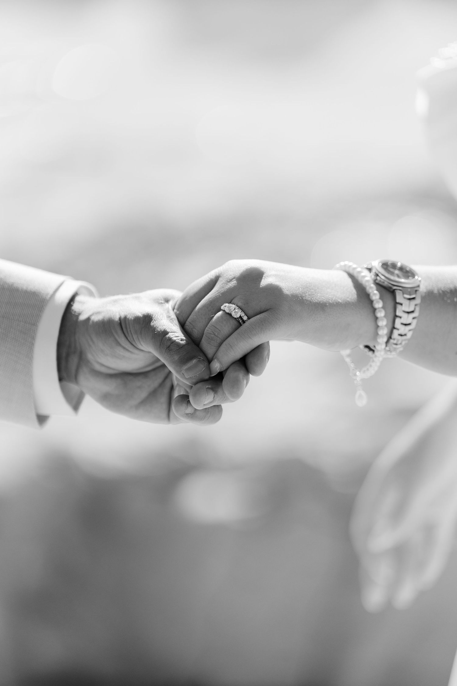 Black and white close-up of bride and groom holding hands showing wedding rings.