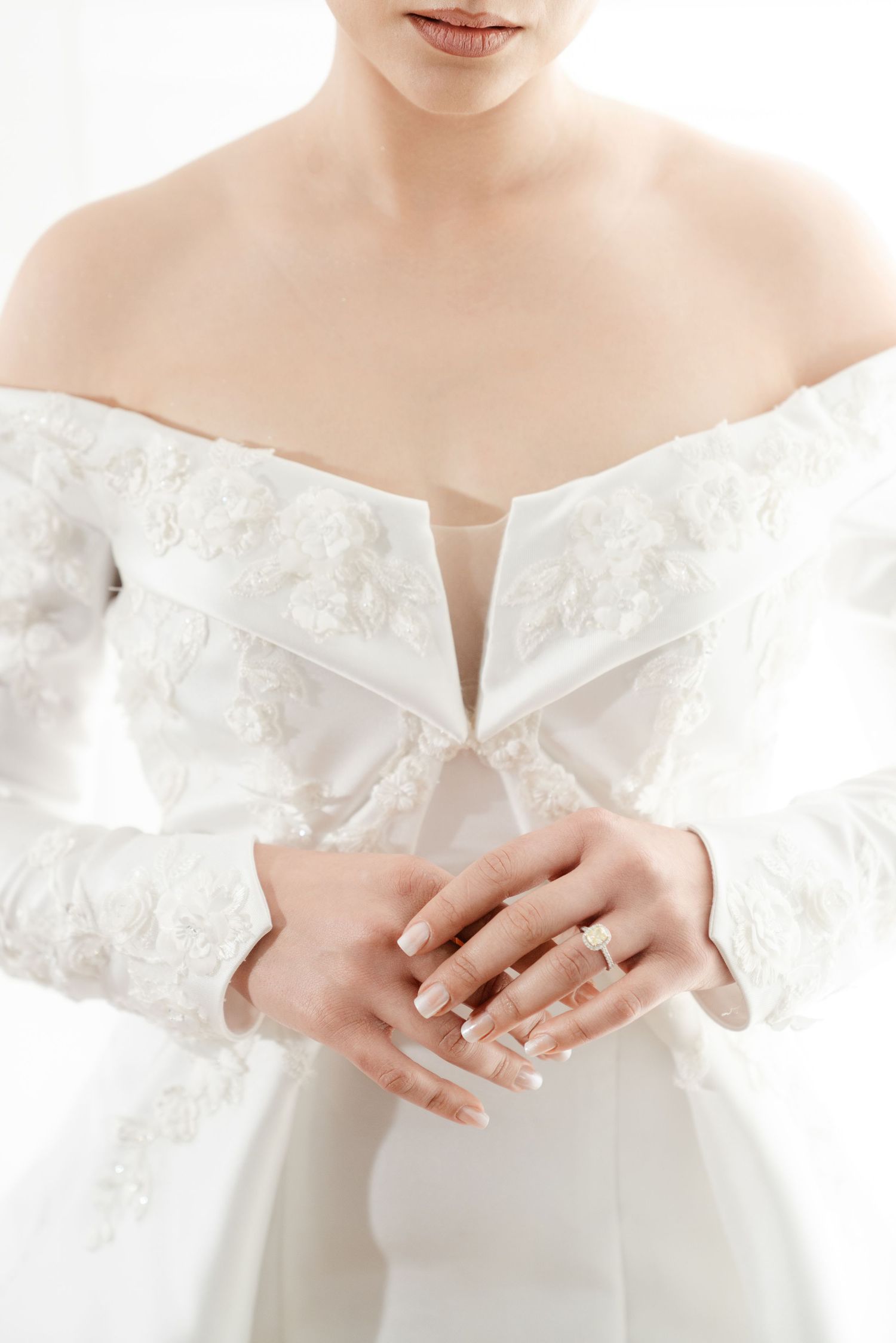 Close-up of bride in off-shoulder lace wedding dress showcasing engagement ring on hands.