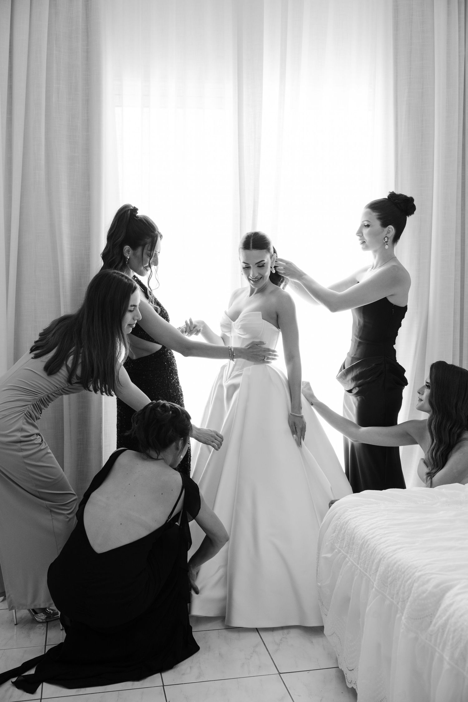 Black and white photo of bridesmaids helping bride get ready before the wedding.