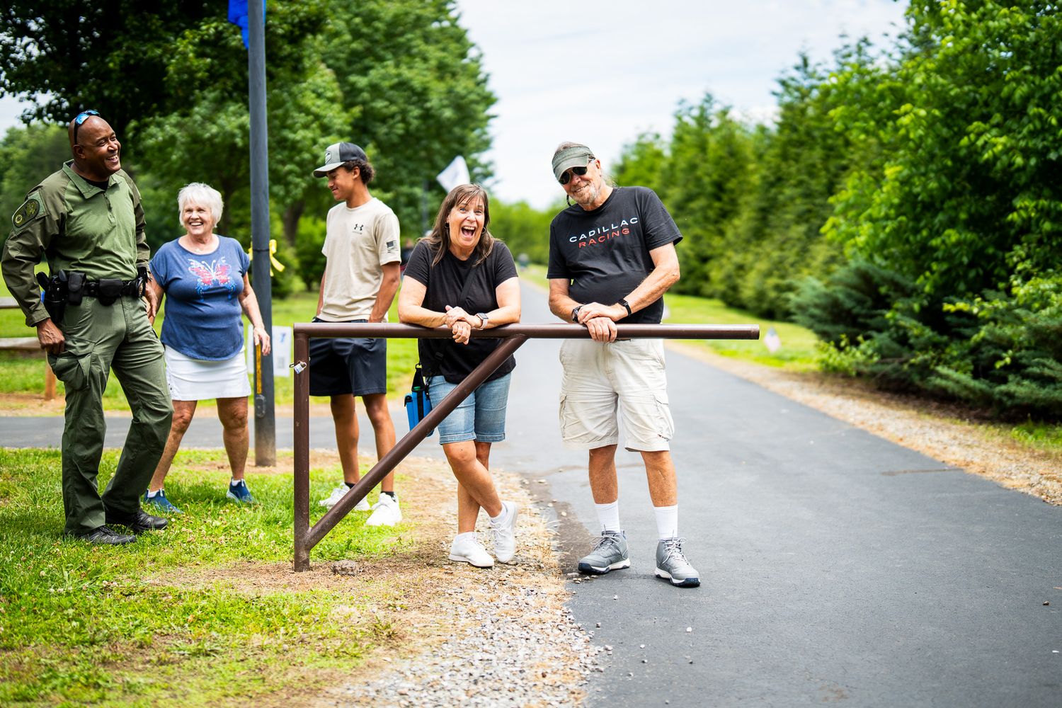 A group gathers outdoors on a paved trail surrounded by lush greenery on a summer day.