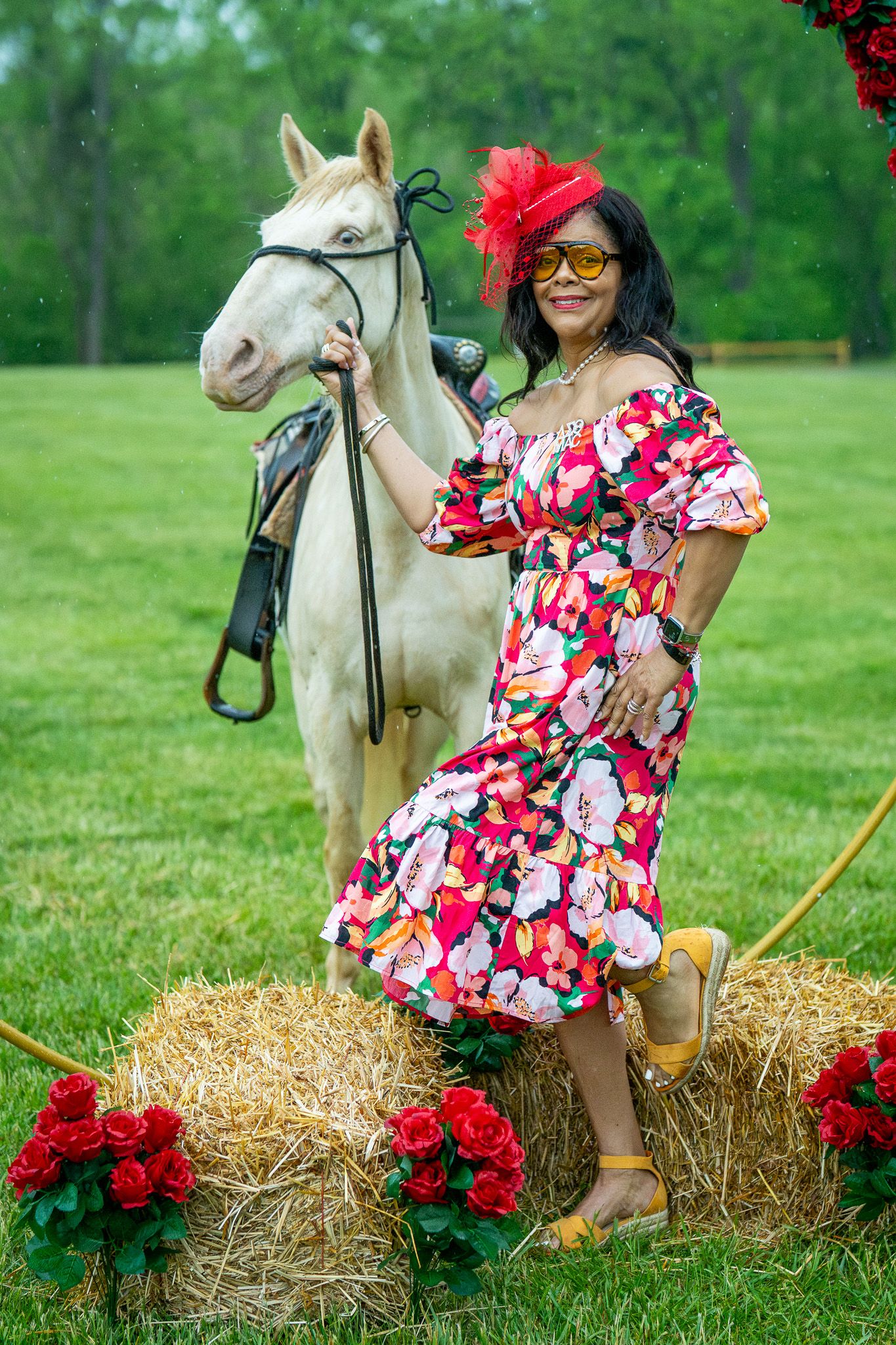 An elegant scene at a derby event with a white horse and colorful floral dress against a lush green backdrop with hay bales.