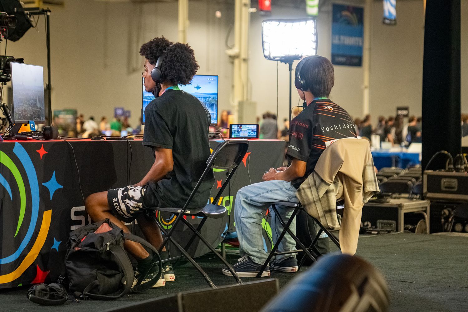 Gamers and spectators gathered at an indoor esports tournament with tables and gaming setups.