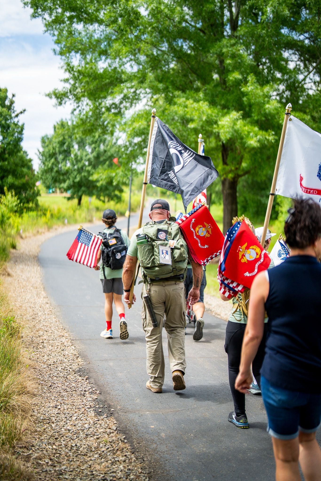 Group of veterans walking along a path carrying military flags and banners during a memorial event.