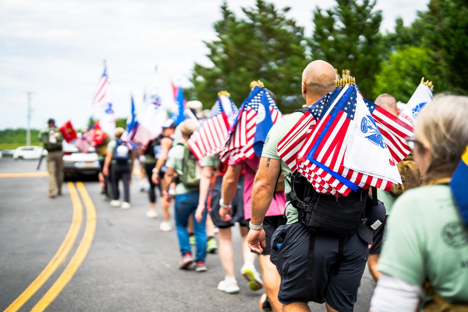 People line a street waving patriotic American flags during a parade celebration.
